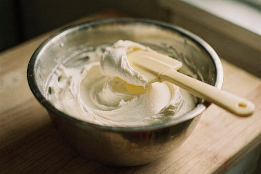 Whipped body butter in a stainless steel mixing bowl with a spatula