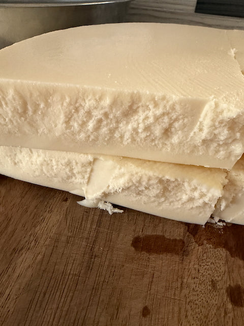 Round cake of white rendered beef tallow broken into pieces on a wooden cutting board