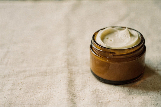 Beef tallow body butter for your face in an open amber glass jar on cream linen