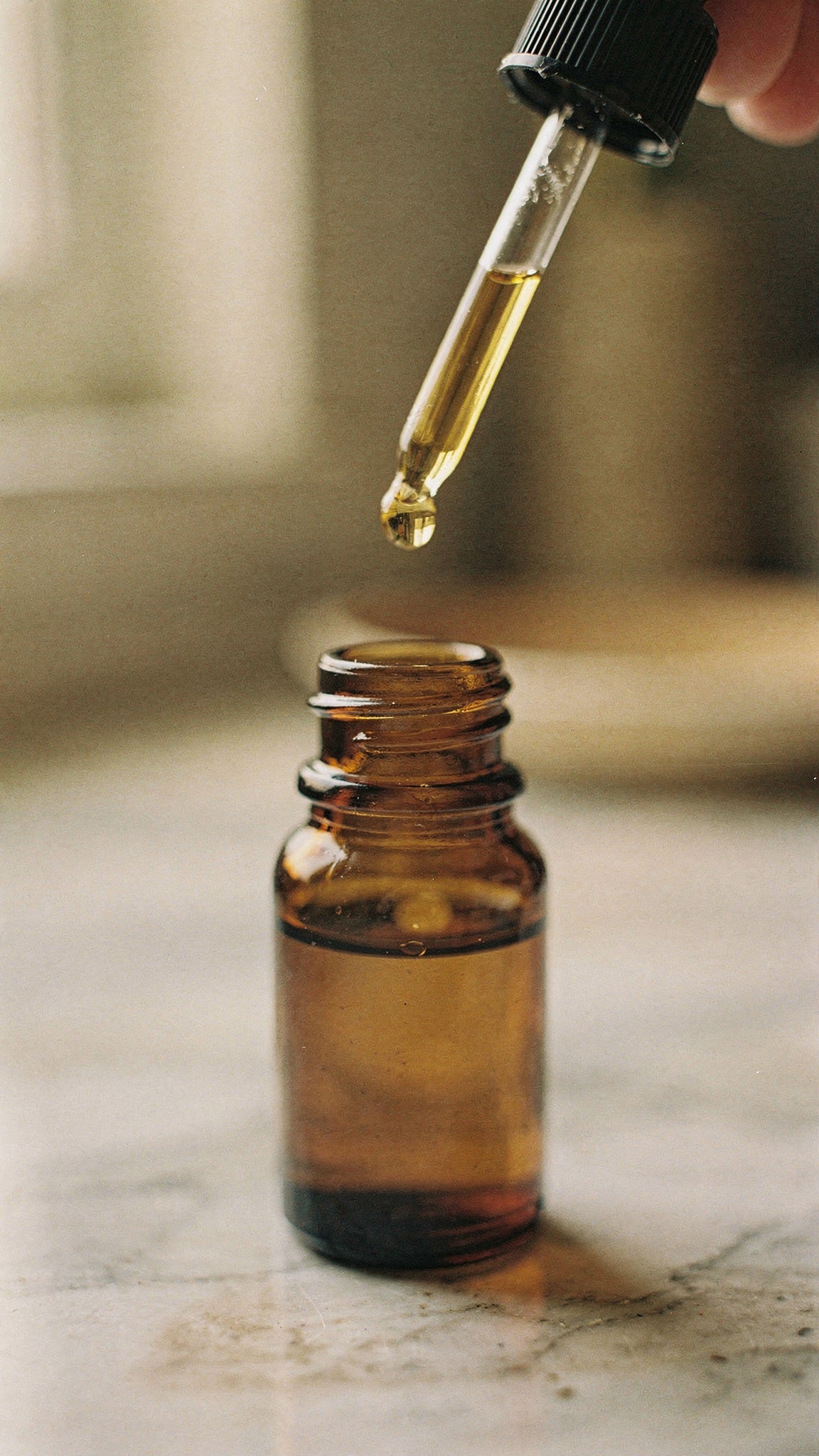 Vitamin E oil for skin, a golden drop hanging from a glass dropper above an amber bottle.