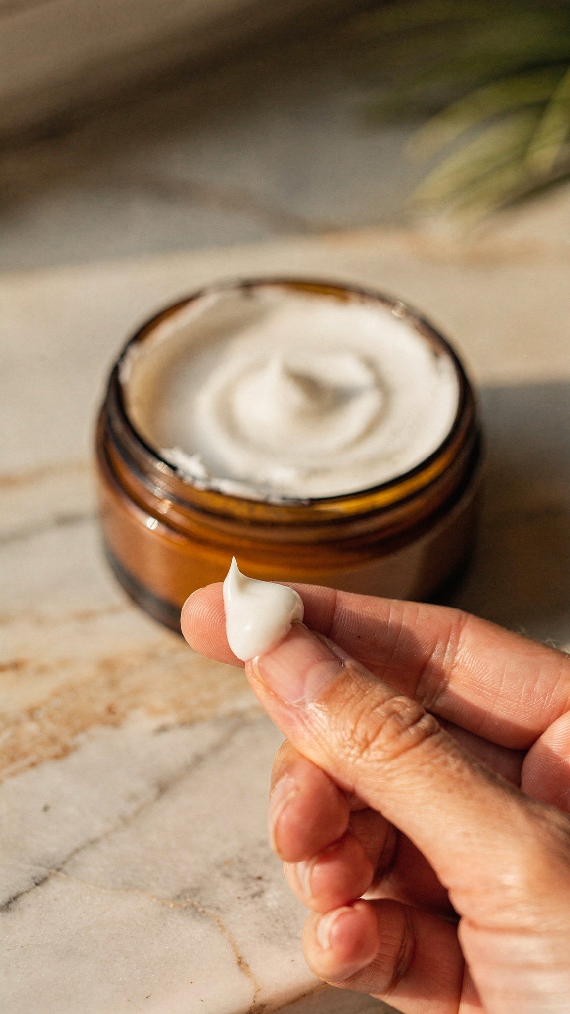 A pea-sized dab of whipped tallow balm on two fingertips beside an open amber jar.