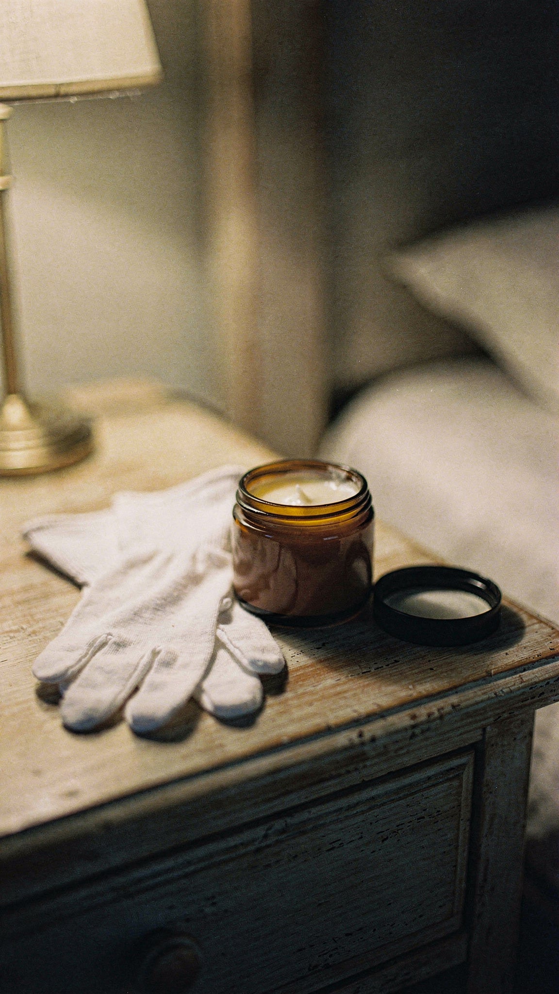 Cotton gloves beside an open jar of tallow body butter for overnight dry skin care.