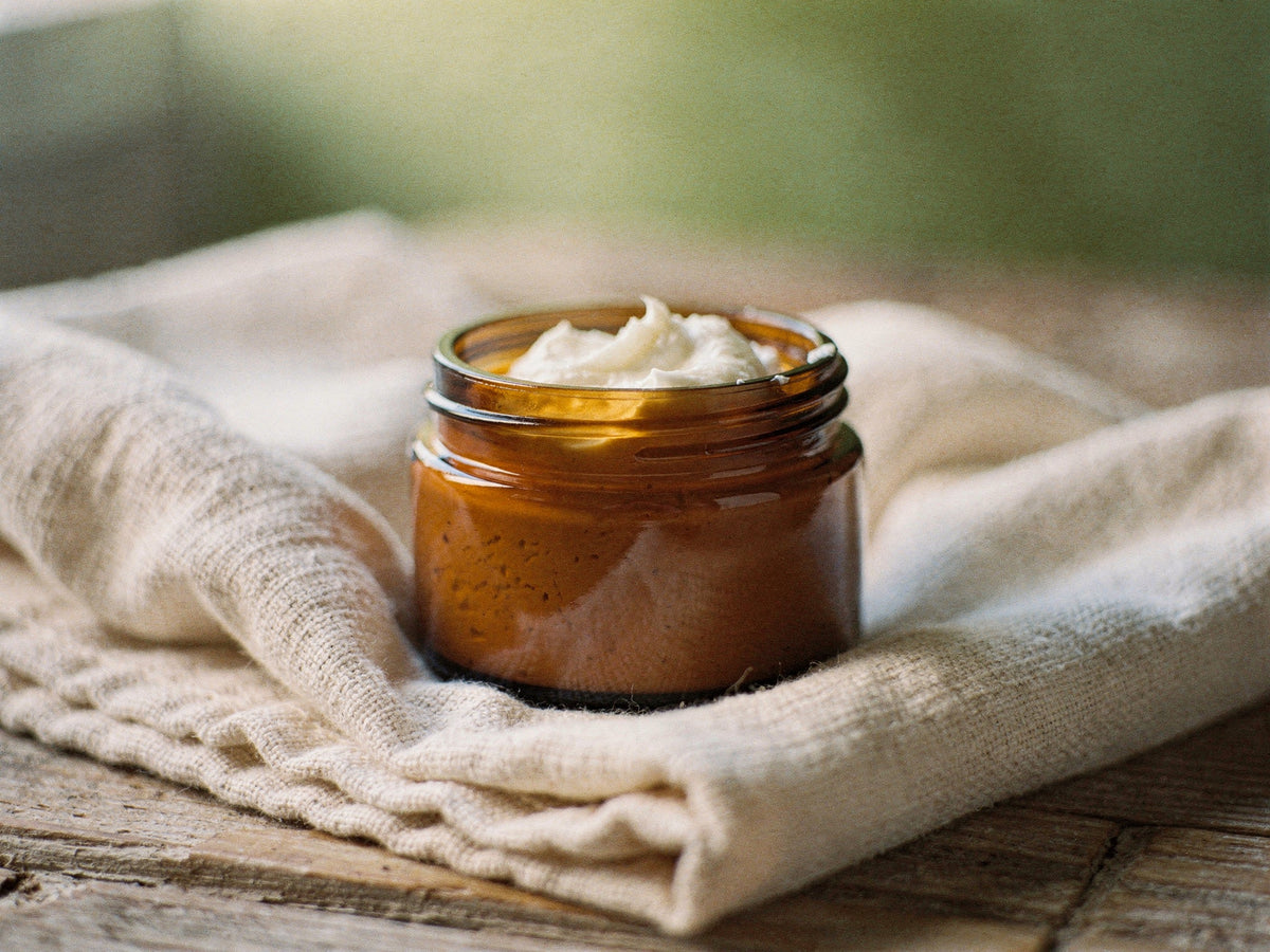 Plain white whipped tallow body butter in an open amber jar, lid resting beside it.